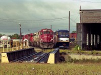 Soo 6039 is an SD60 coupled with another SOO engine and CP Rail units beside CP's Quebec Street roundhouse.<br>
At least one new GMDD F59phi is alongside, CDTX 2002 in the Amtrak California colour scheme.<br>
The Esso tank truck could be delivering diesel fuel; it is close to the fueling area.
