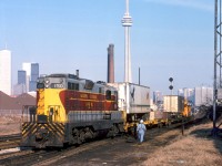 More leased power on CP, this time in the form of Algoma Central GP7's! In late 1978 / early 1979, CP leased a pair of GP7's from Algoma Central, units 150 and 154. Photos show they saw service mainly in the Toronto area, including working locals and transfers around Parkdale Yard, and operating on the Cobourg Turn out of Agincourt (one even made it up the Orangeville and Owen Sound Subs). CP got their hands on them sometime during (or before?) December 1978, and they had gone off-lease at the end of March 1979. CP would later come knocking again in the 80's and lease some of ACR's SD40-2 units.<br><br>Here, ACR GP7 150 handles some piggyback traffic (transfer from John Street downtown?) at the south end of CP's Parkdale Yard, by the Strachan Avenue grade crossing. Note the C&NW "Falcon Service" pig on the first flat, and CP caboose 437086 bringing up the rear. One can pick out the usual downtown Toronto skyline features including the TD Centre buildings, CN Tower, Wellington Destructor smokestacks, and in the distance CP's Tecumseh Tower (that controlled movements from CP's Parkdale Yard across CN's Weston Sub to the Simcoe/Wellington freight shed lead). Strachan Avenue was still a <a href=http://www.railpictures.ca/?attachment_id=15195><b>similar gritty scene in 2007</b></a> (and that old yard lighting tower on the right was still there!), but today it's been radically altered with a giant trench under the road for the Strachan Avenue grade separation.<br><br><i>Keith Hansen photo, Dan Dell'Unto collection slide.</i>