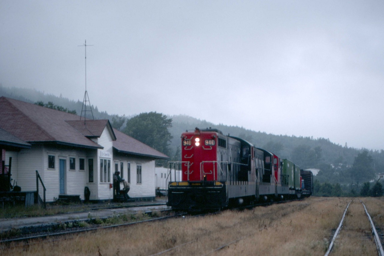 Train 204 pulls up to the station in Clarenville to change crews for the final time as it crosses Newfoundland from Port Aux Basques to St. John’s.  On Thursday morning, August 26, 1982, the train is running some four hours late.  Perhaps the delay led employees in Bishops Falls, the previous division point, to overlook setting off coach 760.  The coach had travelled overnight next to van 6069 from Corner Brook, the next division point to the west.  The car provided accommodation for passengers wanting to experience the Gaff Topsails, a vast wilderness area in central Newfoundland.  

Train 204 is powered by NF210 units 940, 941 and 921.  The CNR, in collaboration with their manufacturer, GMDL, in London, Ontario, specially designed these 1200hp units and their NF110 precursors for service in Newfoundland.  With a 567 series V12 diesel, outside frames and C-C trucks, they proved a reliable and economical replacement for steam power on the 3’6” gauged system.   The two leading units were from the final order delivered in January 1960, while the 921 was from the first order delivered in August 1956.  A museum has preserved class GR-12x 940 at Whitbourne, 54.5 miles west of St. John’s.  The two other units found homes on the Ferrocarril de Antofagasta a Bolivia in Chile as their 1425 and 1419.   Exporail, in St-Constant, Quebec has preserved coach 6069 (CC&F 1949), and van 6069 (NSC/CN 1-1967) found a home in Lewisporte, Newfoundland and Labrador.   

The station at Clarenville, 131 miles west of St. John’s on the 548-mile line to Port aux Basques opened in 1898.  Operator Lindo Palmer formally closed the station for Terra Transport, CN’s successor in Newfoundland, on Tuesday, October 18, 1988.  It has since reopened as part of a museum that includes NF110, 900, 176, the last diner built in Canada by National Steel Car in 1958 and caboose 6061.
