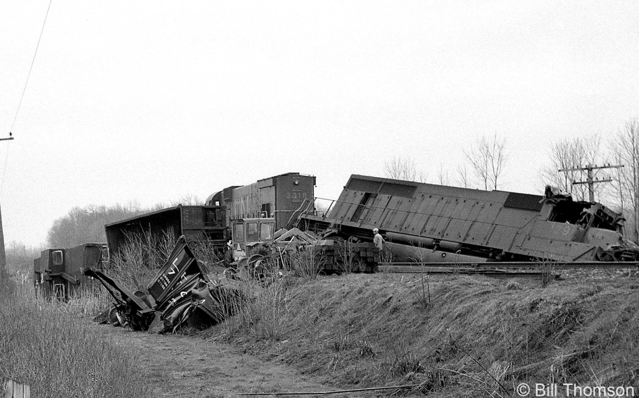 Cleanup efforts are underway on the aftermath of a wreck at Fort Erie, showing CN M636 2318 and an SD40 (possibly 5029) off the rails and with its cab ripped open. A few cars and caboose are visible in the adjacent ditch.