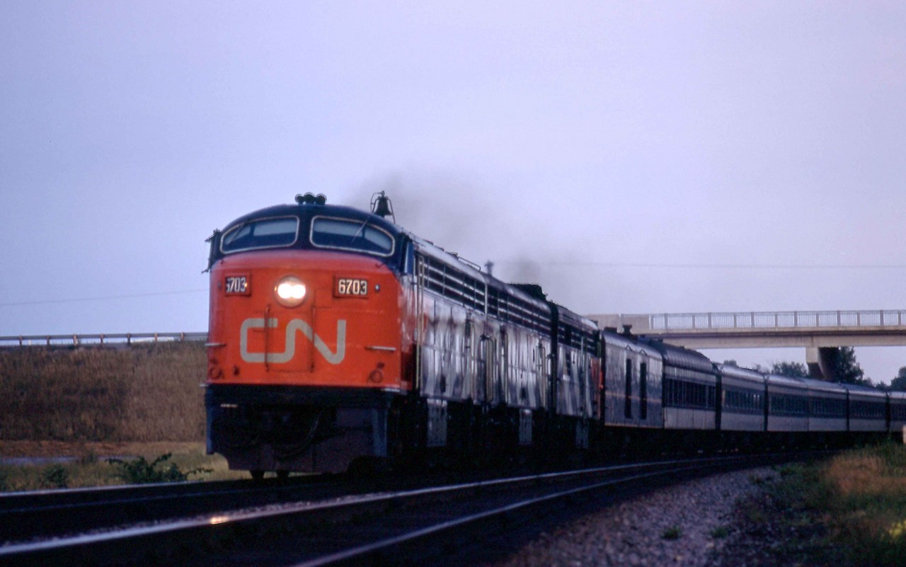 Drumming in the distance suggested that CLC-FM's were on CN Train 55, the Lakeshore.  Sure enough, not one but two CLC passenger units were in charge of the Montreal - Toronto train on the evening of Monday, August 21, 1967, just east of the station at Marysville, Ontario.  Marysville is at Mileage 207 of the Kingston Sub while the train is passing under Kings Highway 2.  The trailing units were CPB16-5 6804 and MLW FPA-2u 6759.  Train 55, the Bonaventure, was due at Belleville, Mileage 220.7, at 7.15 p.m., having left Montreal at 3.35 p.m. and, the previous stop, Kingston at 6.28 p.m.  It was due in Toronto at 9.20 p.m.  The Bonaventure was one of five daily Montreal - Toronto trains in the busy Centennial Year that attracted world-wide visitors to the Expo 67 World's Fair site in Montreal.    

CPA-16-5 6703 was part of six A-B sets purchased by the CNR from the Canadian Locomotive Company in nearby Kingston.  A pair of CPA24-5s, 4801 and 4802, toured the CNR beginning in August 1950 as Fairbanks Morse started its effective control of CLC.  (After the tour, FM sold the demonstrators as New Haven 790 and 791.)  Although GMD and MLW also provided demonstrators around this time, no order was forthcoming from the CNR for passenger units until 1954.  CLC was modestly successful in selling units to both Canadian National and Canadian Pacific.  Amongst other models, the CNR took sixty 1200hp roadswitchers between 1951 and 1956 while the CPR bought fifty H16-44s.   CLC delivered the 6703 in early 1955, and it became the last active CLC cab unit on CN when it was retired in May 1969.