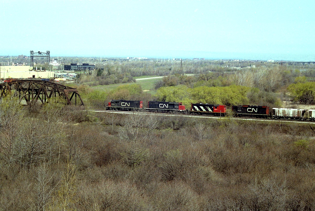 Here's a different angle for a photo of a westward train out of Fort Erie, number unknown, with CN 5509, 5043, 4574 and 4512 up front.
The view is from the hillside at the Walker Quarries, due to foliage and fencing not a location available to us photographers any more. Note the Glendale Av canal bridge is up and a freighter is heading south. I have forgotten whether the train would be stopped, as CN canal Bridge 6 looms straight ahead. The location the train is approaching is known as "CN Iron Bridge" for obvious reasons. The view extends out as far as the QEW as the Garden City Skyway can be partially seen at the extreme right. Soft spring foliage add a bit to the colour here.
I had staked out this spot waiting for my own photo version of the new Amtrak Maple Leaf #97, which started up on this day; and the freight was a bonus.