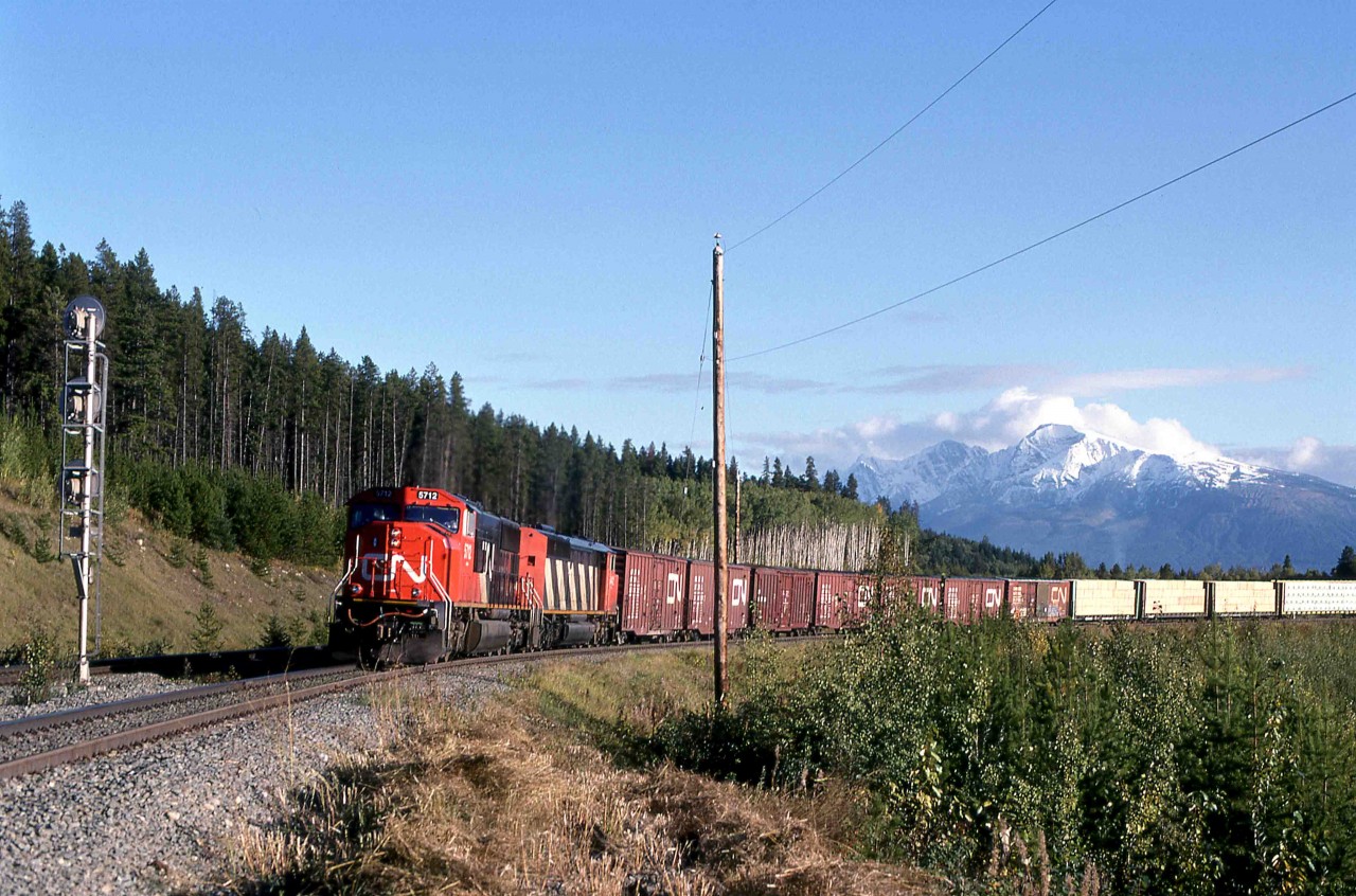 A Canadian National eastbound off the Prince George line is about to enter the Albreda subdivision at Mileage 70.6 Spicer, British Columbia, on September 26, 1997, and continue east towards Jasper.   

Before the construction of new connecting lines in this area, the train would have continued east on the Tete Jaune sub, joining the Montreal - Vancouver line at Red Pass Junction, Mileage 43.7 of the Albreda sub.
New construction eased gradients and allowed movements from west to south.  The new Robson Sub from Taverna, twenty miles west of Red Pass Jct on the Prince George line to Charles, Mileage 71.6 of the Albreda sub effectively created almost 28 miles of bi-directional double-track.  CN also doubled-tracked the Albreda sub for an additional 1.7 miles, almost to the town of Valemount.   

The Grand Trunk Pacific Railway opened the Jasper - Prince George Prince Rupert line in 1914.   The Canadian Northern Railway's line from Edmonton to Vancouver also used the Yellowhead Pass west of Jasper.  This line opened in January 1915.   Their consolidation into the Canadian National Railways led to the early removal of considerable duplicate trackage between Edmonton and Red Pass Junction.  Traffic growth in resource-rich Western Canada led to the installation of lengthened sidings, double track and the new lines near Mount Robson.  

GMDD in London, Ontario, delivered 5712 (#956616-87) as one of 105 SD75Is in 1996 in CN class GF-643a.  Repeat orders in 1997 and 1999 brought the total of these units to 175.   They feature a 16 cylinder 710 series diesel rated at 4,300 horsepower.  The "I" in the model designation indicates the optional "Whisper Cab" that isolated the crew from much track and engine-related vibration.  This feature makes them still popular with trains crews.  The SD75Is were the first units purchased by the newly privatized CN.