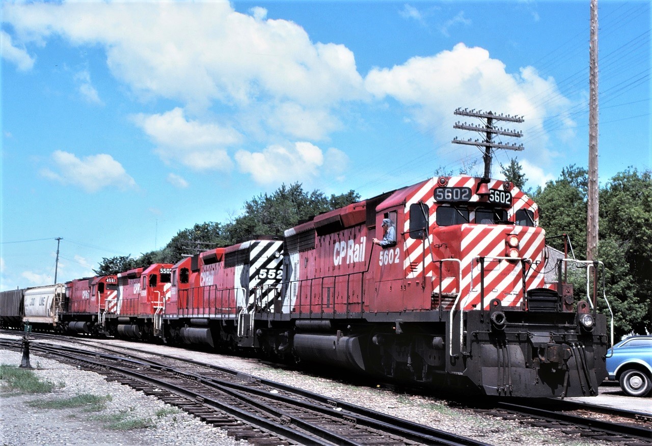 The engineer of an outbound grain train patiently waits for the headend brakeman to return after completing their double over prior to heading east.  Six-axle GMD and MLW units were common on the prairies during the 1970s.