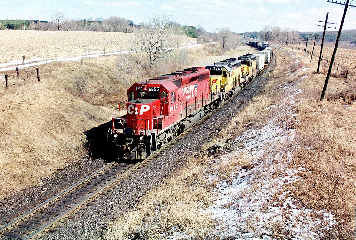 After being slightly delayed by the morning Woodstock Job switching in the yard, a westbound with CP 5655, 5431 and 5428 are accelerating up the grade out of Woodstock as they approach the Highway #2 crossing on the Galt Subdivision. Prior to being acquired by CP both 5431 and 5428 were former GATX leasers, then prior to that were Union Pacific as they originally were built for Missouri Pacific and obtained through the large UP/MP merger.