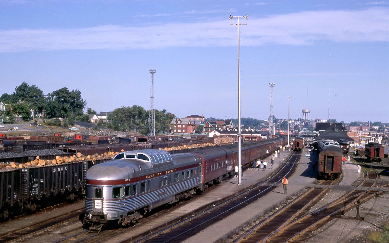 The Paris Street overpass in Sudbury, Ontario, provided an excellent vantage point to witness the combining of the Montreal and Toronto sections of CPR passenger trains.  On Sunday, August 20, 1967, I was on hand to enjoy the various switching moves as the Expo Limited took the scheduled 45 minutes to prepare for its 8.35 a.m. departure for Vancouver.  Later in the day, I would see the splitting of the Canadian into its Montreal and Toronto sections.  

Budd sleeper-dome Banff Park is prominent in the foreground as a yard crew working with S-4 7092 has prepared the rear of the train for departure.  Mate 7090 worked the coaches on the west end.  In the distance, connecting RDC-2 9100 would depart as Train 427 for Sault Ste. Marie.   

Although I did not record the consist, CPR's Assignment of Space booklet confirms that the Park car would continue from Montreal to Vancouver.  The Montreal train also included a 10-6 homebuilt Grove series sleeper, followed by an N, S or T series 12 section-1 drawing-room car, and an R series 8 section, 1 drawing-room, 2 double bedroom car.  Then a 12-1 sleeper such as Scotstown, which S-4 7092 had just set off after its trip from Montreal.  An A or W series heavyweight diner from Montreal would turn back to that city on Train 6.  Toronto cars arriving on Train 15 included an R series car and two 12-1s for Vancouver.   

The switcher marshalled the Toronto cars ahead of the R series sleeper from Montreal.  An A or W series diner just ahead of the Grove car would continue from Toronto to Winnipeg and a replacement provided for the remainder of the run to Vancouver.  In Winnipeg, a switcher placed a 500 series Skyline cafe dome between the sleepers and coaches.   The stopover in Winnipeg also saw the addition of another Grove series sleeper for Vancouver.  Finally, in Regina, an R car series car was added for Vancouver.  In both cases, the switching placed the sleeper immediately behind the Skyline.  

Three of CPR's newest mechanically air-conditioned 2200 series coaches rode on the head end behind a 4700 series baggage car.  Typical power from Montreal to Calgary was two boiler-equipped MLW RS-10s or FPA-2s.  The Toronto leg drew a similar, single unit.  A pair or trio of boiler-equipped GP9s was normal west Of Calgary.  

The overall effect was a one-season re-creation of CPR's classic Dominion, which had crossed the country in heavyweight style on a four-night schedule for decades until Monday, January 10, 1966.   The Expo Limited was part of the CPR's celebration of Canadian Confederation.  Another significant contribution was the Canadian Pacific Pavilion at the World's Fair, Expo '67 in Montreal.  The Expo Limited not only served tourism in the Canadian Rockies but took travellers to Expo '67.  It was a grand year!