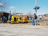 Many local residents of the town of Palmerston watch the rail removal process as several pieces of CN track equipment were slowly following the rail train as the crew worked to remove pieces and loosen sections of the rail for the retrieval process. Earlier that day, the rail train had gone through the town for the last time and was powered by CN GP9RM’s 4115 and 4140. During April 1996, CN had removed the last sections of the Newton and Owen Sound Subdivisions that remained between Harriston and Stratford. 