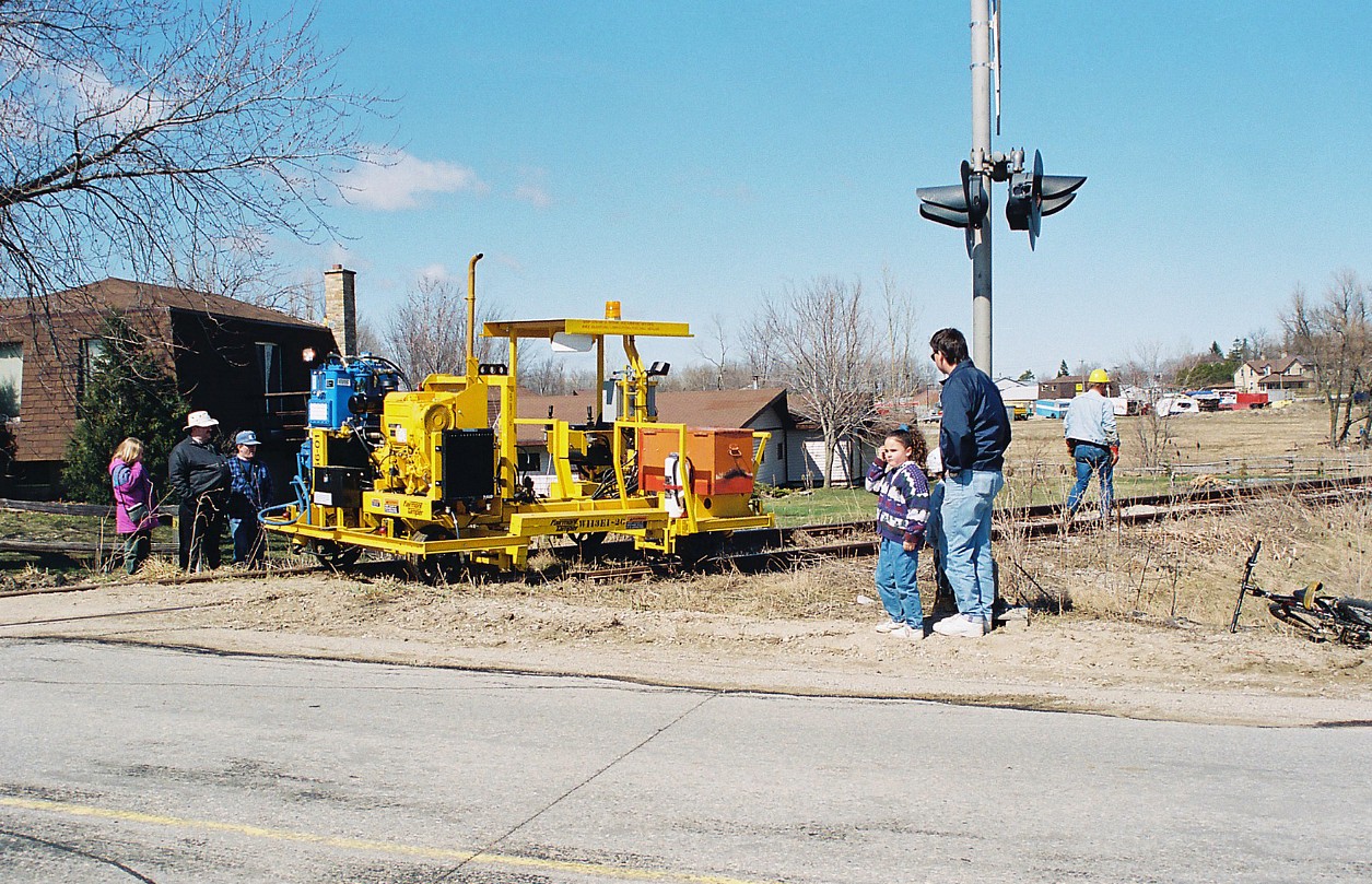 Many local residents of the town of Palmerston watch the rail removal process as several pieces of CN track equipment were slowly following the rail train as the crew worked to remove pieces and loosen sections of the rail for the retrieval process. Earlier that day, the rail train had gone through the town for the last time and was powered by CN GP9RM’s 4115 and 4140. During April 1996, CN had removed the last sections of the Newton and Owen Sound Subdivisions that remained between Harriston and Stratford.