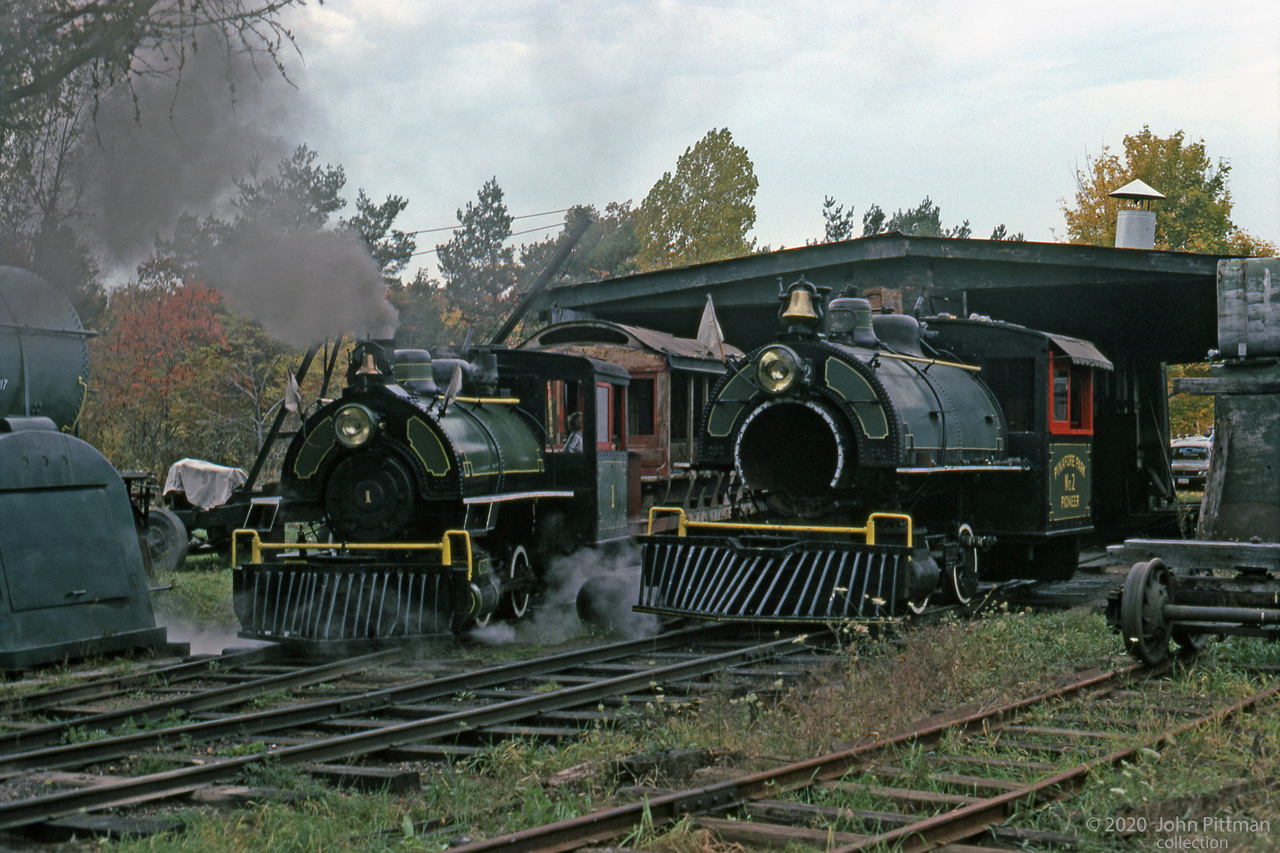 Pinafore Park RR 0-4-0 saddle tank engines #1 and #2 at the engine shed in Pinafore Park, St.Thomas ON.
20 October 1979 was an autumn Saturday; this could be morning before rides begin.
#1 is in steam, with 2 children visible in the cab.
#2 named "Pioneer" is non-operational this day, with its left-side rods and smoke box door off.
The engines were acquired from the Huntsville and Lake of Bays portage railway after it closed down in 1959.They were later re-sold, returning to Huntsville in the late 1990's.
More information with other railpictures.ca images, RL Kennedy's "Old Time Trains", or by web search.