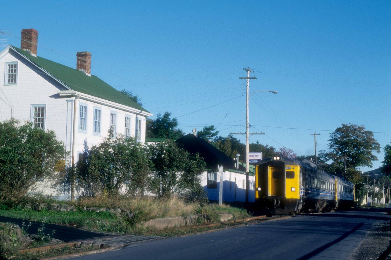 VIA Train 152,the Evangeline, is running alongside First Avenue as it departs Digby, Nova Scotia at, 8.30 a.m. in September 1989.   Just a few months away, on Saturday, January 13, 1990, the train would make its last run followed by its Sunday only counterpart, Train 154, to round out passenger service in Western Nova Scotia.  The train had departed Yarmouth, 86 miles west of Annapolis Royal at 7 a.m.; Digby was at Mileage 20.2 of the Yarmouth Sub.  The Train would cover another 151 miles before arriving in Halifax at 12.35 p.m. where it would make connections for Montreal, Sydney and other maritime communities.  

The Western Counties Railway had completed a line from Digby to Yarmouth in August 1879.  In the early days, the Joggins, Bear and Moose rivers prevented the completion of a through-line to Halifax.  The Missing Link, as it was known locally, between Digby and Annapolis Royal, was filled by steamboats.  In 1890, the Missing Link was finally closed with federal financial assistance.  The Dominion Atlantic Railway purchased the Western Counties in 1893 and merged it with lines east of Annapolis Royal to provide a through route.  Ironically, the end of VIA service led to the railway's abandonment west of New Minas in April 1990.   Once again,  the Bear and Moose river crossings were expensive to taxpayers as they paid the cost of their removal in 2013.   

VIA 6221, was built in July 1956 (serial 6301) as MKT 20, their only RDC-3 although it lacked the customary RPO section.  The Katy purchased it to provide a connection from Wichita Falls, Texas, to their Texas Special train at Denison.  C&O acquired the car in November 1960, and it served as a backup to their two ex-M&StL RDC-4s along the Big Sandy between Ashland and Elkhorn City, Kentucky.   The B&O borrowed the car and, CN purchased it in August 1965 and renumbered it as D-356, later 6356.    VIA rebuilt the car as an RDC-2 and renumbered it 6221.   Industrial Rail Services of Moncton bought the car in 2000.  They could not find a buyer and scrapped the car in 2016.