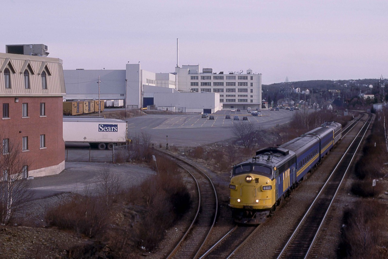 Moncton bound Via Train 613 is about to scoot under the overpass on Mumford Road in Halifax, Nova Scotia.  It had just left the Armdale station in the background at 5.25 p.m. in late March 1989.  At the time, VIA was short of the RDC's customarily assigned to this service and employed some conventional equipment including, GMD and MLW cab units.  The FPA-4s ended their service at the end of the month as they were not retrofitted with Reset Safety Control as mandated by Canada's National Transportation Agency.     

CNR 6505 (GMDL 11-1954 #A-635) was part of the railway's initial order for passenger units, 28 A-B pairs in early 1954.  It became VIA 6505 on Friday, March 31, 1978.  Later, VIA sold it on Wednesday, March 8, 1995, for use on the Conway Scenic Railway.  Pan Am Railways bought the unit for its executive train and renumbered it PAR 1.  

Much has vanished from this scene in the last thirty years.  The rail-served Sears distribution centre has become a Walmart on the lower level and a Sobeys supermarket on the upper level of the West End Mall.  Sears, formerly, the Simpsons store in the background, has been transformed into an office complex while Sears has withdrawn from retailing throughout Canada.  The Sears siding formerly gave access to the Scotia Railroad Museum just to the left of the fencing.  Also, CN removed the inbound double main track in the 1990s.   With all the changes around the city, the vantage point remains one of only a handful in Halifax, where one may easily get a photograph of an entire passenger train coming and going.