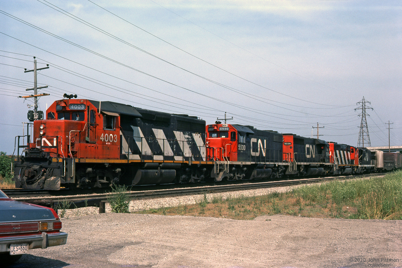 Five different types of GMD locomotive power this CN train on the Grimsby sub in mid-July 1980.
Leading is CN 4003, second CN GP40 in the series built 1966; it would be renumbered CN 9303 in 1981.
Second is GP38-2 CN 5530 built 1973, it would be renumbered CN 4730 in 1988.
Following are SD40 CN 5036, GP40-2(w) CN 9650, and GP9 CN 4535.
Based on current streetviews, looks like this train was heading west toward Hamilton.