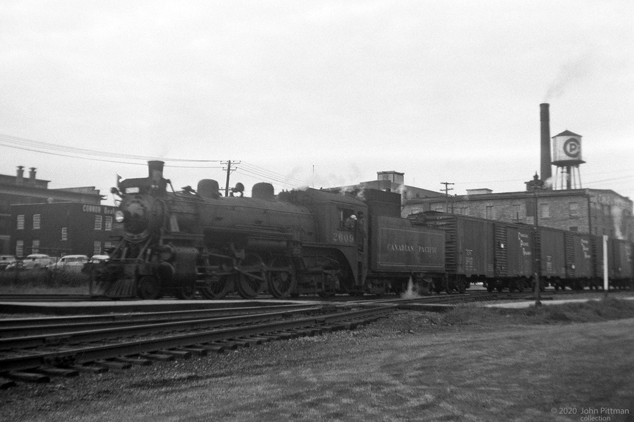 Canadian Pacific has stopped beside a different CP.
CPR Class G2 4-6-2 CP 2609 was photographed in Hull Quebec at Canada Packers (their CP on the water tank).
Visible part of the train is 40 foot steel boxcars, the ubiquitous car of the era that carried most non-perishable freight that fit inside. 
Once the more industrial neighbour of Ottawa across the river, in 2002 Hull was amalgamated with other nearby  Quebec communities, becoming the downtown of the city of Gatineau.
Sources indicate Canada Packers used to be on Rue Montcalm in Hull.