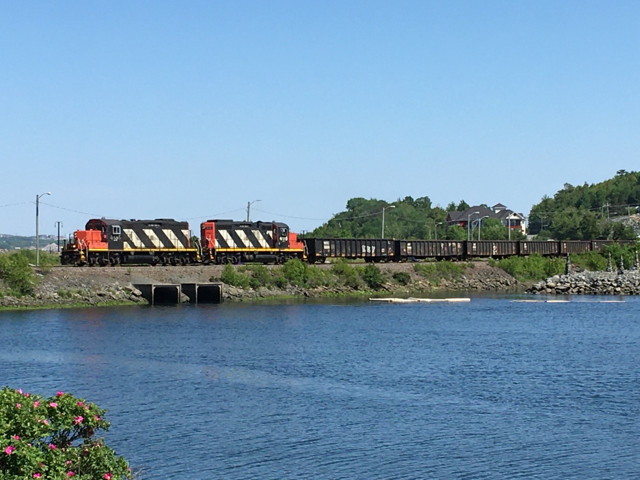 Marilynn Linley's image shows CN local 519 heading west at Moirs Mills in suburban Halifax.  Moirs Pond is in the foreground.  The train was outbound from Rockingham Yard to Milford with a cut of gondolas for gypsum loading at the National Gypsum mine at Mileage 36.6 of the Bedford Subdivision.  Marilynn shot with her cellphone at  3.53 p.m. on Thursday, June 18, 2020.   It was our first train sighting in over three months since we saw CSX GE 5355 on a local in North Carolina.  

I did not expect that our trip to our grandaughter's drive-by birthday parade would include a train, so the Nikon stayed in Port Lorne.  We did make planned stops at Costco and Starbucks.   

The local featured two classic CN locomotives, both remanufactured GMDL GP9s from the late 1950s.  The CNR bought the leader, 4135, as GR-17h class 4528 in 1957 and remanufactured it at their Point St. Charles Shops in Montreal in 1991.   Designed for road switcher service, in class GR-418f, it's driving position was reversed to a short-hood-forward orientation.  CN rebuilt forty-four similar units between March 1984 and May 1991.    Between September 1981 and 1984, CN similarly rebuilt thirty-seven other GP9s in the 4000 series.  The earlier rebuilt units were 9,000 pounds heavier.  The trailing unit, 4115, was formerly GR-17u 4322 of 1959.  CN assigned it to class GR-418d.