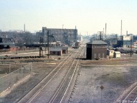 The CN-CP West Toronto diamonds in "The Junction" are pictured in 1963, looking east from the nearby Weston Road overpass. A short local lead by a CP Alco/MLW switcher is visible on the north mainline of the North Toronto Sub, near the switch to the MacTier Sub that headed north out of town for northern Ontario and the west coast. The West Toronto interlocking tower is prominently pictured on the south-east quadrant, and controlled movements through the junction via a <a href=http://www.railpictures.ca/?attachment_id=28987><b>manual interlocking system</b></a> (note the rods and linkages running from the base of the tower and along the tracks to control wayside signals and switches). The tower would be demolished next year in September 1964, and Centralized Traffic Control (CTC) installed and active by March 1965. A number of section houses dot the northeast quadrant opposite the tower.<br><br>West Toronto was a main junction point for CP's lines leading north, east, and west out of the city of Toronto, as well as the location of their West Toronto & Lambton yards and locomotive servicing facilities. <br><br>The closest track crossing CP's North Toronto Sub is CP's MacTier-Galt Sub connecting track, used regularly by the "The Canadian" between Toronto and Sudbury (via the MacTier Sub that lead north out of town) until the passenger train was rerouted by VIA the late 70's.<br><br>The CP's Galt Sub is visible on the <a href=http://www.railpictures.ca/?attachment_id=15874><b>lower right</b></a>, coming up from downtown Toronto (Union Station, and CP Parkdale Yard) and curving west to lead out of the city for Streetsville, Guelph Junction and lines beyond. <br><br>The two mainline tracks running alongside the tower and crossing the diamond are for <a href=http://www.railpictures.ca/?attachment_id=19407><b>CN's Brampton Sub</b></a>, which was their mainline from Toronto to Stratford until it was reorganized in January 1965. The Toronto-Halwest (near Bramalea) section became the Weston Sub, and after many decades this set of diamonds was grade separated in 2014.<br><br>The furthest track crossing at the diamonds on the other side of the tower is the lead from the CP MacTier Sub to the <a href=http://www.railpictures.ca/?attachment_id=38483><b>"Old Bruce" service track</b></a> that ran down the east side of the corridor to Dundas Street, serving local industries.<br><br>CP's North Toronto Sub disappeared in the distance and cut through Toronto to Leaside, the Belleville Sub, and Agincourt (home of CP's new Toronto Yard that was under construction, opening next year). The opening of Toronto Yard meant much freight traffic and transfers would use the line between the two yards, and also to access the MacTier Sub and Galt Sub leading north and west out of town.