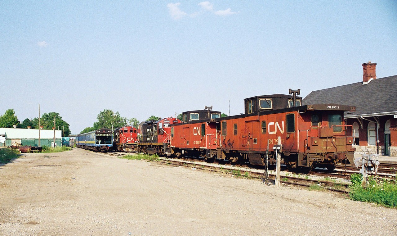 An eastbound CN business train powered by CN GP9RM's 7082 and 7083 is slowly departing Kitchener, revealing the CN local assigned units and cabooses at the time. They included; CN GP9RM's 7031, 7030 and cabooses 79817 and 79513 seen in evening light across from the VIA Rail station.