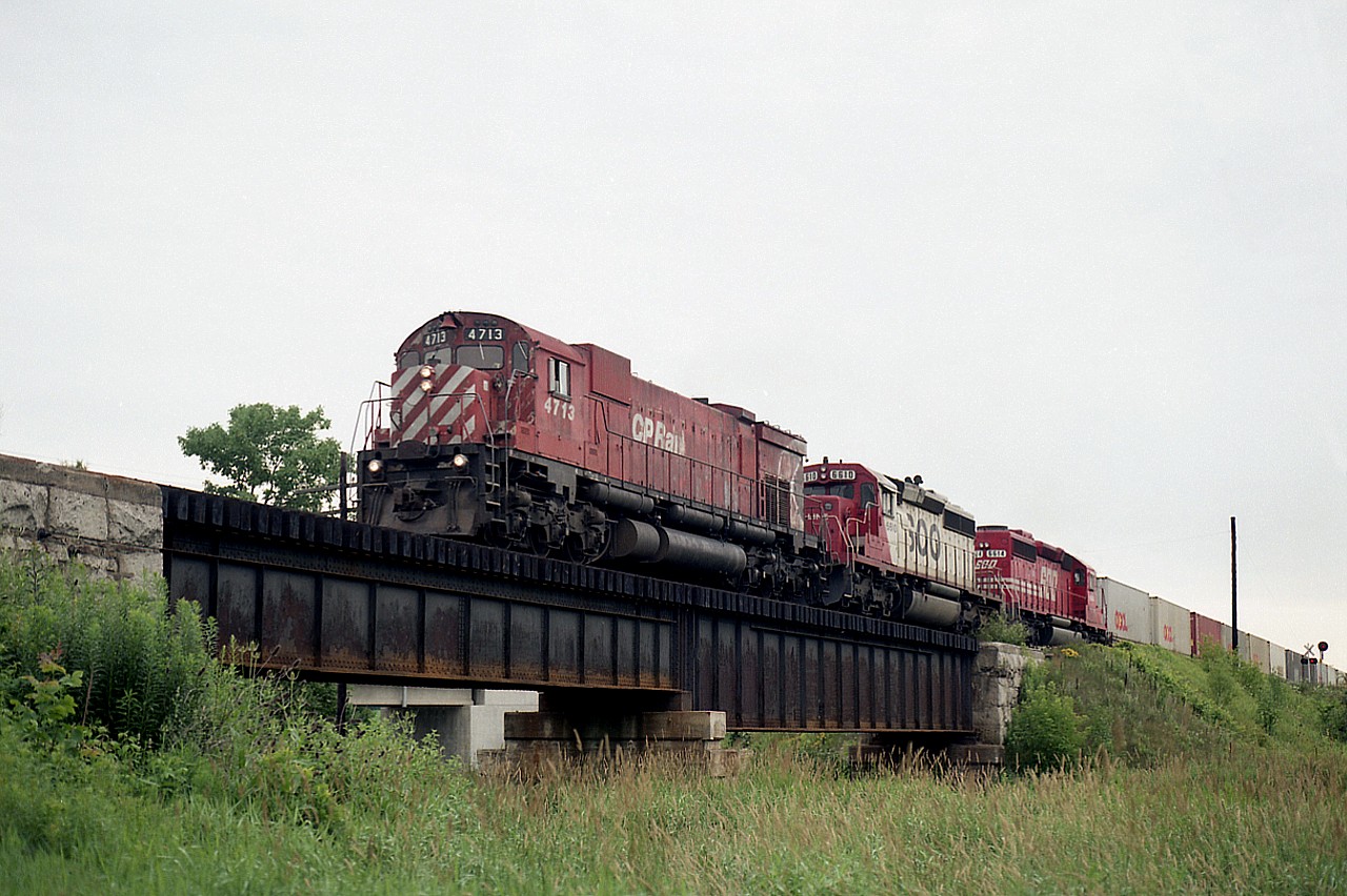 Doesn't look much like a bridge from this angle; and in reality when you are there it doesn't look like much either. Little clearance over the water. But this is the Thames River, and on the right you can see the crossing for Township Road 6. We're just south of the village of Innerkip.
It was nice to catch a big M-636 leading, as they were beginning to be retired and were not very common at the time. ("Un"-retiring of many in 1994 gave us new life on the hunt for these, fortunately.)
So, this is CP 4713 with SOO 6610 and 6614 westbound on a rather dull day of flat grey skies. Nice train.