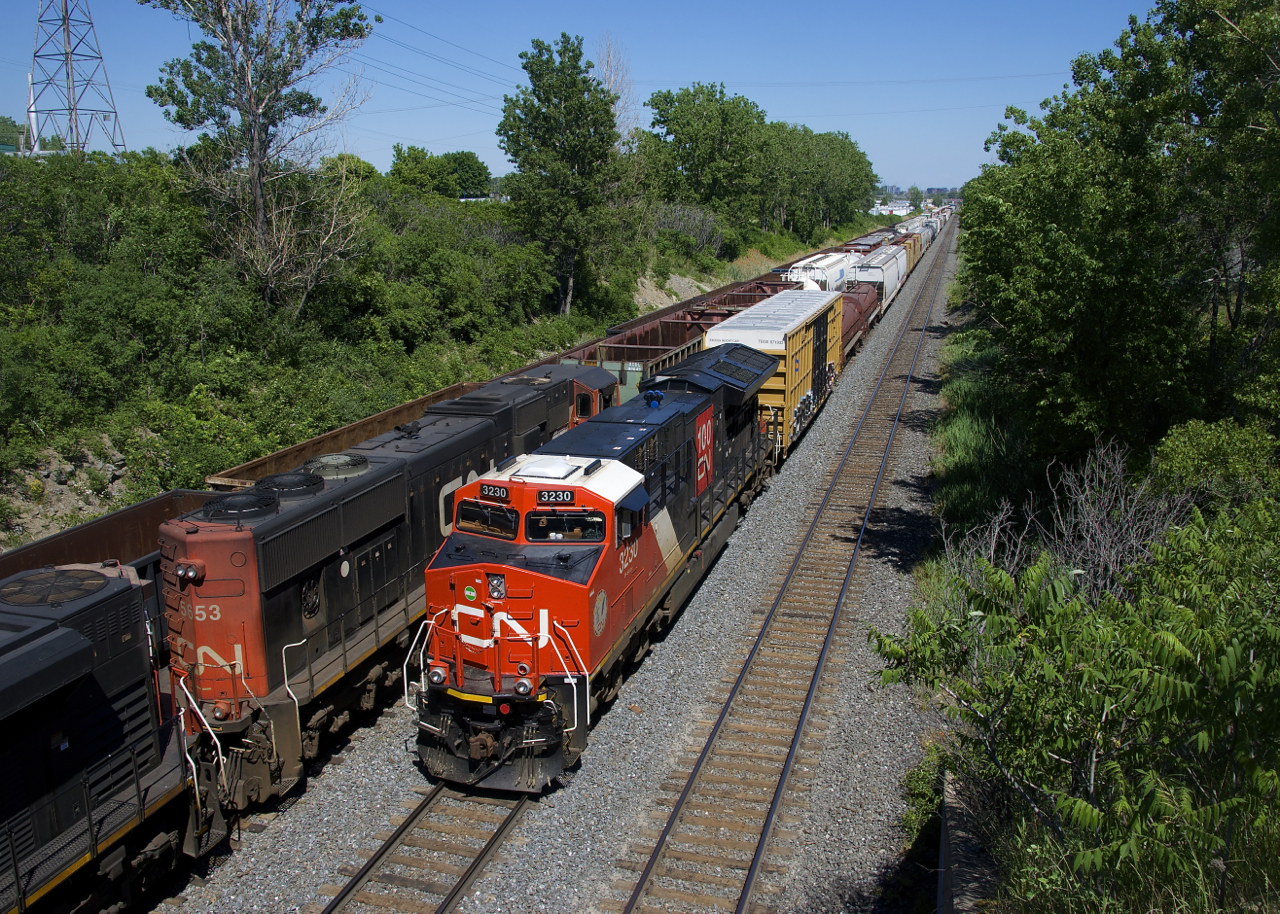 CN 3230 brings up the rear of CN 322 as it passes CN 527 at left. CN 527 is awaiting its signal to get into Taschereau Yard, while CN 322 has just left the yard after setting off all the cars that were behind the DPU. CN 322 will terminate at Southwark Yard, about a dozen miles from here.