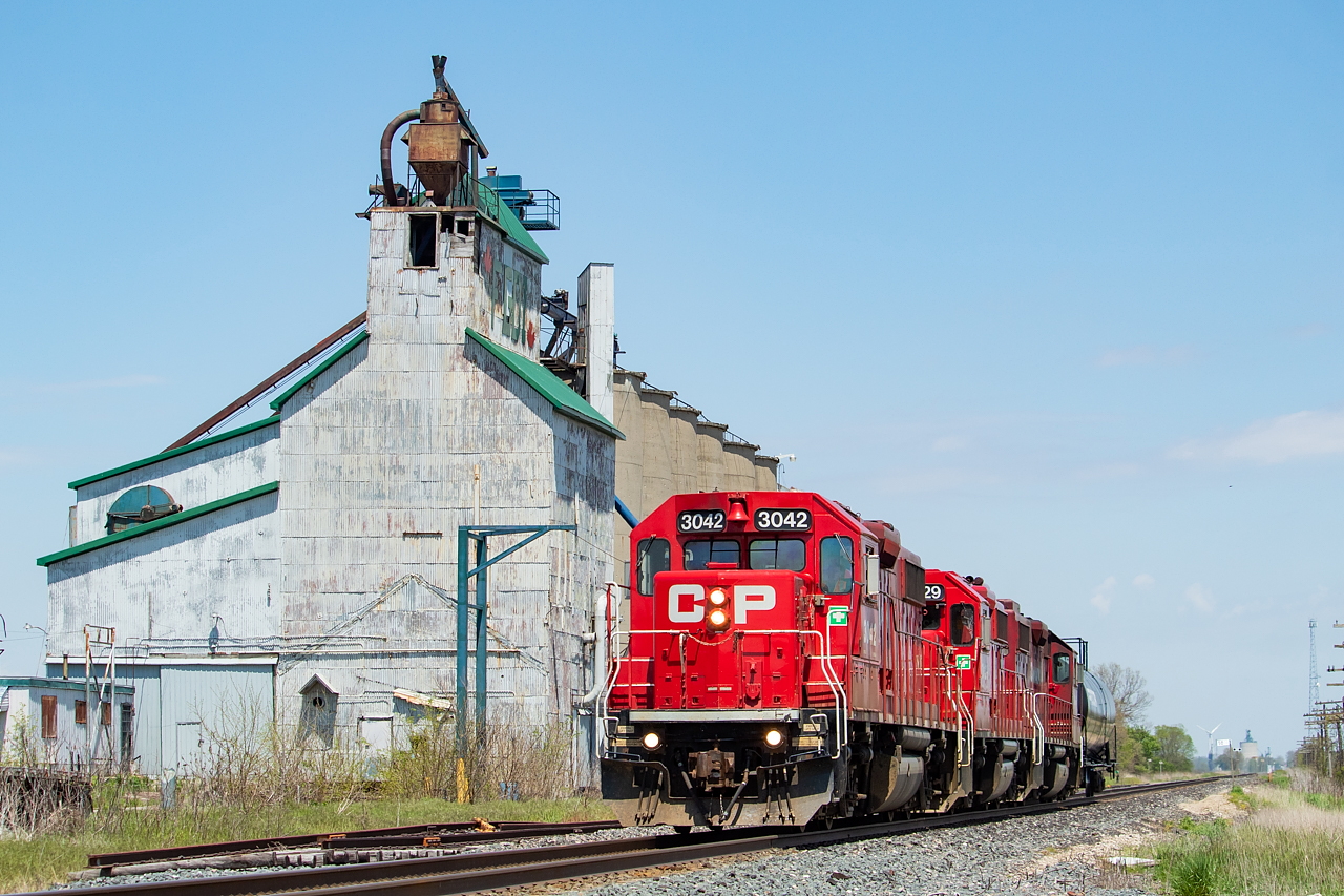 A trio of GP38-2s provides the power for the day's T29 as it blasts past the old elevator in Arkwood, doing a healthy 60 mph. This elevator is hard to find history on, but from what I can tell, it last operated in 2013. The letters at the top, FGDI, stand for Farmers Grain Dealers Inc., though the elevator passed through several owners in its life including Taylor Grain. There were three tracks here - the main, a siding, and the track that serviced the elevator itself. As you can see the siding is cut off, but it still has two derails on it. The tracks up to the elevator are still there but are slowly being buried over time. And the switch to that track to the elevator is still in place off the siding. Way off in the distance you can see the still active elevator in Kent Bridge.  Other RP contributors have posted shots here in the past, including Hunter Holmes, Jay Butler, and Mike Molnar. On this particular day, T29 had one tank for the ethanol plant in Chatham. They'd leave the tank on the main at Ringold, run around it, and tie back on before working the plant then heading back home to London.