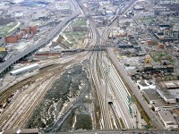 Here's the aerial view of the downtown Toronto railyards, as seen looking west from the CN tower in April 1987. The whole area has and was undergoing many changes: by now many tracks of CN's Spadina Coachyard (bottom left) were either vacant or removed altogether, as VIA had moved their passenger train servicing to the new Toronto Maintenance Centre at Mimico, and all the old downtown railway lands were prime real estate for redevelopment. CN's Spadina Roundhouse (out of frame at the bottom) had also been vacated and would soon be replaced with the Skydome.
<br><br>
In the centre of the image is Bathurst Street bridge where the western rail lines of the Toronto Terminals Railway from Union Station split into the CN Oakville Sub, CN Weston Sub, and CP Galt Sub. The industrial pre-gentrified Liberty Village is visible above the junction (note the bright blue building along Strachan Avenue, part of the old John Inglis factory). Next to it is CP's Parkdale Yard, by then converted into a container-handling facility (full of blue CAST containers).  The Massey Ferguson plants can be seen in the upper right of the photo, a series of manufacturing buildings clustered in the Strachan/King area that once manufactured farm equipment that was shipped out by rail.
<br><br>
On the upper left are the CNE grounds, and below that the Molsons Brewery, a large brown brick building served by rail (accessed via the CP "Wharf Lead" from Parkdale Yard, seen running on an angle across the top of the image above Inglis). Just below is the CBM/St. Mary's Cement Fleet Street plant for local concrete distribution (also served by rail). Along Bathurst Street below the Gardiner Expressway are two warehouses for Loblaws. Equipment from the displaced Canadian Railway Historical Association's former harbourfront museum is visible out back, stored on the spur leading from the old harbourfront trackage that had been removed (included is CN switcher 7988 restored in old orange and black paint, later scrapped).
<br><br>
Along the bottom right of the image is Spadina Avenue, with Front Street at the lower right. "The Globe" lettering on the roof of the old Globe & Mail headquarters is visible (demolished in more recent years). GO Transit commuter trains are stored at the Bathurst North Yard, once a CN freight yard. The CP "shed lead" spur that started under Bathurst St. bridge and ran up to street level at Front & Spadina to access the old freight sheds still appears to be intact.