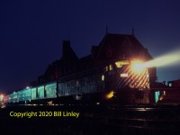 Ninety Years of Service <br> <br>

CPR E8A 1802 graces the headend of Train 41, The ATLANTIC LIMITED, at McAdam, New Brunswick, at 10 p.m. on Sunday, June 3, 1979. <br> <br>  

The westbound Saint John to Montreal train had covered the 84.4 miles of the McAdam Sub and will depart at 10.10 p.m.  It will follow the Canadian Pacific's "Short Line" through northern Maine that had opened to passenger service exactly ninety years before.  Note the ninety affixed to the anticlimber.  The opening of the 479-mile Short Line made the CPR a line from sea to sea across North America.  It was not so until December 1974 when CP Rail purchased the Maine Central line from Mattawamkeag, 56.1 miles to Vanceboro, Maine.   Previously, they had enjoyed trackage rights. <br> <br>   

E8A 1802 was one of three ordered by the CPR in September 1948 as an E7A to match the diesels of the Boston & Maine on their shared service between Montreal and Boston.   The CPR changed the order, so EMD delivered the E8 in December 1949 after E7 production had ended.  When RDCs replaced conventionally powered trains on the Boston run in 1959, the CPR transferred the E8s to other routes.  Some of these included Toronto - Windsor, Toronto or Montreal to Sudbury and, later, Montreal to Quebec City and Ottawa.  As these services wound down and following the demise of 1801 in a collision, the two remaining units found a home for most of the 1970s on the ATLANTIC LIMITED.  Their twin boilers and prime movers provided a desirable reserve and ended the usual practice of assigning two units during winter. <br> <br>

The makeup of this train was the same as it had been for most of the 1970s. The four cars included baggage 2767, 4-5-1-4 sleeper GRANT MANOR, Skyline dome 505 and coach 123.  On this trip, GRANT MANOR had replaced DRAPER MANOR, which ran with regularly with 505 and 123.  Senior conductor George Draper out of Montreal reportedly often arranged its reinstatement when 'his car' was not in the consist.   On the other set of equipment was CAMERON MANOR, long associated with baggageman Dave Cameron.  This sleeper usually ran eastbound on the rear behind Skyline 515 and coach 119. <br> <br>  

The two dome cars were specially fitted with walkover seats in the dome section so that passengers would not have to ride backwards.  On the other hand, crews switched, not turned, the cars so that the sleeper ran backwards behind the baggage car on the westbound trip with the coach on the rear.  As CP became disenchanted with passenger service in the 1960s, it is remarkable that they did not discontinue the train nor replace it with a Rail Diesel Car. Despite often very low revenue passenger counts, it continued as a full-featured daily train until VIA upgraded it and extended it to Halifax, Nova Scotia, on Sunday, October 28, 1979 as their ATLANTIC. <br> <br>  

Behind the train, W. H. Painter's Chateau style station-hotel of 1901 dominates the scene.  The station supported the intense traffic generated at the junction of CPR lines to St. Andrews and St. Stephen to the south, and Edmundston to the north.  It featured a 20-room hotel on the second floor, station services on the ground floor including a restaurant and coffee shop behind the E8.   The Canadian government designated the station as a National Historic Site in 1976 and a Heritage Railway Station in 1990.  
