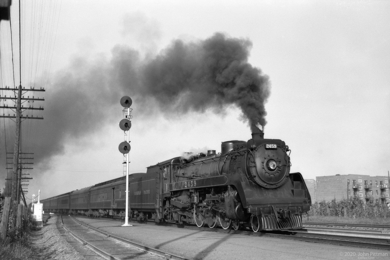 CPR 4-6-2 class G3h engine 2459 leads a passenger train on Montreal Island on 28 August 1951. 
Later colour images show it with grey boiler jacket and tuscan red tender side and below the running board.  
Based on data for sister CP 2461, probably built by CLC Kingston in March or April 1945. 
Quoting from R.L. Kennedy's website "Old Time Trains": 
These "Twenty Four Hundreds" (actually, 2351-2472) were very capable locomotives built with one piece cast bed and multiple throttle. They were as different as day and night compared to earlier G3's 2300- 2350. 
They were considered the best steam locomotive on the CPR, true dual service freight or passenger engines with 75 inch diameter drivers. They were the only class painted in either freight black and/or passenger tuscan red. 
I believe that this is a westbound afternoon train from Windsor Station approaching Montreal West station. 
One of the low-rise residential buildings cropped off at right had "Westhaven Village" on it, as if to advertise. 
Westhaven Elmhurst Community Rec Associaton maps nearby, and very similar buildings can be found here in streetviews.  
Signal M44 is gone, but "42" signals are on a signal bridge a bit further east. (CP Westmount Sub MP 4.2)