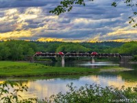 A late train 406 crosses the trestle at Hammond River, New Brunswick with the sun slightly visible near the treeline. 