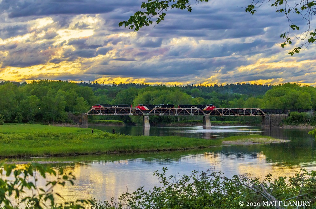 A late train 406 crosses the trestle at Hammond River, New Brunswick with the sun slightly visible near the treeline.