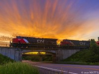 With a colorful early morning sunrise, CN train 121 is westbound, hauling out of Moncton, seen here getting up to speed at Berry Mills, New Brunswick. Half of the train is made up of empty well cars. 