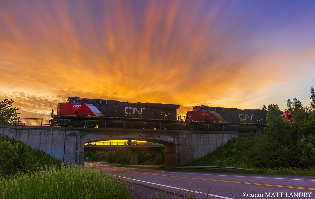 With a colorful early morning sunrise, CN train 121 is westbound, hauling out of Moncton, seen here getting up to speed at Berry Mills, New Brunswick. Half of the train is made up of empty well cars.