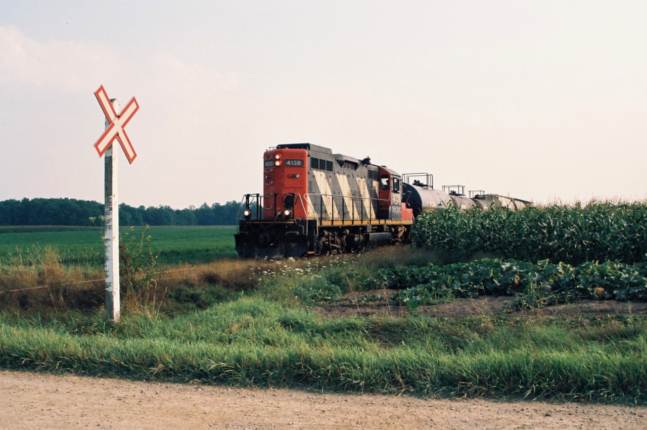 In July 1993 I was invited for my first cab ride by the crew of the 15:30 Kitchener Job. They would be taking a train north to Elmira on the Waterloo Spur, which was only a block away from my house at the time. The crew said they would get me at the crossing as they headed-up. For a 13-year-old kid, there was no greater excitement than knowing that this time I wouldn’t just be watching from the sidelines, but actually on board this day. CN GP9RM 4138 slowly came into view as it led the small train across the two streets ahead of mine. Once the train came to a stop, I climbed aboard before being handed a bottle of cold water as it was an incredibly sweltering afternoon. Rollie, who was the conductor, let me have his seat as we began across my street and towards Uptown Waterloo.
 

The entire trip lasted about two hours as the job switched Nutrite Feeds and Sulco in Elmira after arriving. I took photos of as much as I could. Seeing things from high in the cab gave a new perspective on the line. The friendly crew even took photos of me in the engineer’s seat as well. So many wonderful memories were made that day, however, in the end that’s all that became of my first cab ride on the spur….just memories. Unfortunately, it was later discovered that the roll of film in the camera wasn’t advancing at the time while the number counter was, giving the illusion of things working properly. It was my first hard lesson in photography, to ensure all equipment was fully functioning and working properly before a shoot.
 

While time had continued on in the following years, I was always still determined to photograph 4138 on the Waterloo Spur again to somewhat make-up for the photos lost from that day. I had to wait over three years, until September 1996 when CN had assigned 4138 to Kitchener again. On a hazy late summer afternoon, my dad and I followed the 15:30 Job up to Elmira and back. Here, 4138 is seen emerging from a large corn and vegetable field as it approached Scotch Line Road south of Elmira with cars for Nutrite as well as Sulco Chemicals. However, the GP9RM looked a lot different from three years prior as it no longer had any CN logos….