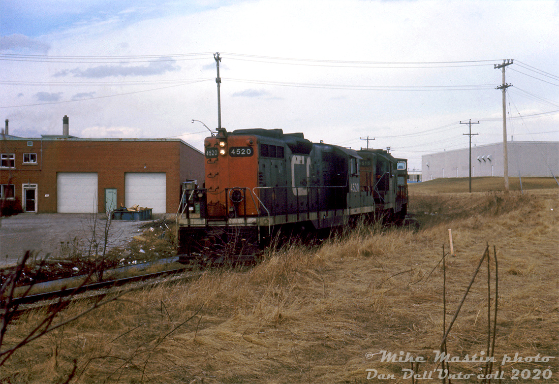 After finishing up their duties further up the line, CN GP9's 4520 and 4515 head south on the southwest leg of CN's GECO Spur (or GECO Branch) in Scarborough, coming around the bend at Milne Ave. crossing while enroute back to the Kingston Sub with a lone caboose in tow.As mentioned in a previous photo, the CN's GECO Branch/Spur was constructed to serve the "Golden Mile" area of Scarborough during the post-war industrial boom, as the area formerly inhabited by a World War 2 munitions plant transitioned to domestic manufacturing, and the surrounding farmer's fields were gobbled up by the urban sprawl of the suburbs. Part of the line was partially built over the old abandoned Canadian Northern right-of-way (that ran north of CN's ex-GTR Kingston Sub). Industrial decline and gentrification in the 90's/2000's resulted in a lot of the factories being redeveloped into neighbourhoods and townhouses, the loss of rail customers, and today only a portion of the GECO Spur remains to serve the few remaining rail customers. This portion from the Kingston Sub to near the TTC's Warden Subway Station had been removed and the land sold off.Mike Mastin photo, Dan Dell'Unto slide collection.
