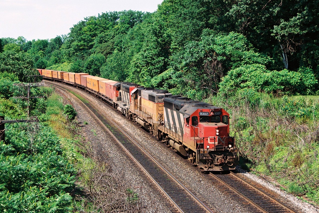 During 1994, CN had acquired 24 SD40-2’s from Union Pacific, that were originally numbered UP 4090-4102, B4103, 4104, 4106-4114. CN quickly temporarily renumbered them by changing the first number to a ‘6 from 4’ to cycle them into service. These units were seen all over the CN network that year and eventually became CN 5364-5387 by 1995 after being remanufactured at AMF in Montreal.

Here is a link to a great photo of a pair of the former UP SD40-2’s on opposite trains taken by Arnold Mooney. HERE 

Here CN train 238 with 9307, a renumbered former UP SD40-2 and a CN GP40-2L(W) are seen heading towards the former Snake Road walk bridge (now named Beth Jacob Court) on the Oakville Subdivision, just east of Bayview Junction.