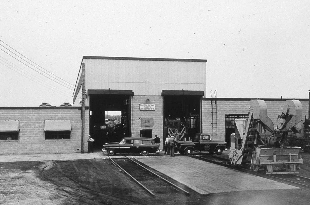 Further to my comment on Liam MacDougall's photo capturing a GO train at Danforth between Main Street and Victoria Park Avenue ( http://www.railpictures.ca/?attachment_id=42149 ), here is a glimpse of the CN Danforth Work Equipment Shop that once occupied the grounds where all the townhouses now sit. This photo was taken on the new shops official opening day of June 5, 1956. The new 'state of the art' facility replaced a much older and smaller facility on the same property. The old shop was built on a foundation that had the large rollup doors into the building at boxcar door/flatcar deck height. It became a small repair and storage facility when the new shop opened. After each season of rail replacement, tie replacement, ballast gangs, surfacing crews, and general Engineering projects, most equipment on the Great Lakes Region was returned to the Danforth shop to be repaired/overhauled for the next production season. Through the 1960's and 70's the yard tracks were home to the fleets of Engineering accommodation and work service cars including red fleet boarding cars, tool cars, coach cars, tanks cars, machinery flats, white fleet units, etc. They were all stored, stocked, and repaired here. With the ever increasing quantity, size and complexity of work equipment machinery, a new repair facility was constructed in Capreol, Ontario in the late 1970's to take some of the workload from the Danforth shops. The value of Toronto real estate made the railway property at the Danforth complex very appealing and the yard, Steel Bridge shop, and once modern Work Equipment shop would soon be gone to make way for the townhomes that are present there today.