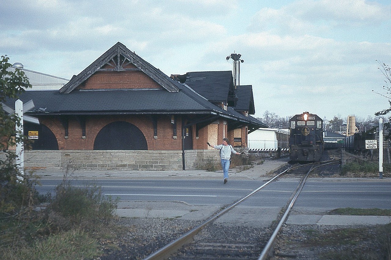 First run of the TH&B Nanticoke train using leased Chessie power. (TH&B was short on power and could not spare units to run this train).
Here we see a crewman running up ahead to guard the Market St crossing as the train creeps slowly ahead. The interesting thing about this location is the old TH&B station on the left. This historical structure was built back at the turn of the century; the closest part 1896 and it was enlarged facing track, far end, in 1906. Closed in 1969, it became Iron Horse restaurant. Suspicious fire in 1982 gutted it. It was rather surprising it was able to be saved judging by the roof damage. But it was reconstructed in 1990 and existed as a steakhouse once again until closing permanently in 2007. The building is currently vacant.
The power on this train is B&0 4815, C&0 3885 and 4828. Since this was November and the sun sets early, it was great to see the train get out of Hamilton at a good pace and the sunset didn't occur until the train was at Waterford, when I called off the chase on a rather entertaining afternoon.