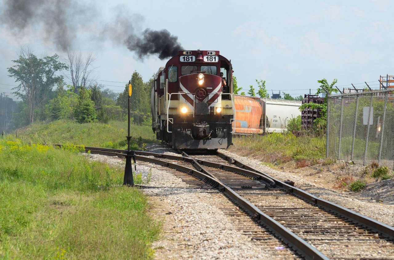181 approaches the switch stand between the GJR South Spur and the CN N Guelph Spur as it pulls a cut of hoppers up the dip from PDI Industries and Traxxside on a hazy hot day. MLW smoke always included