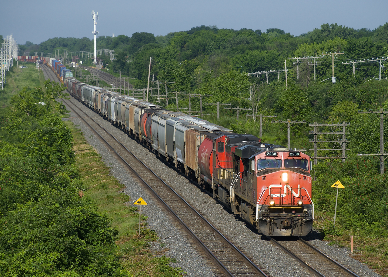 A 610-axle CN 106 heads east with grain up front, followed by the regular intermodal traffic. Power is CN 2238 and CN 2586 up front and CN 8964 mid-train.