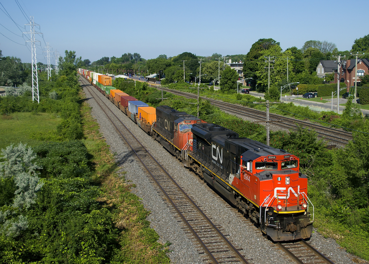 The conductor waves from CN 120 as it approaches MP 14 of CN's Kingston Sub with CN 8944 and CN 5697 power. In a few miles the train will enter Taschereau Yard where cars will be added and the power swapped out for a new set.