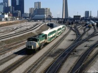 GO Transit GP40-2W 709 trails an inbound commuter train of three bilevels and an APCU (F-unit converted into a cab car/HEP car) heading to Union Station in downtown Toronto, passing by VIA's former CN Spadina coachyard at Bathurst Street. VIA LRC locomotives are visible heading up consists on the yard tracks, and a CN S13 used for switching passenger cars sits in one of the sidings. Self-propelled VIA RDC's sit near the old steam-era coal tower, beyond which is Spadina Roundhouse where VIA's locomotives are serviced.
<br><br>
The 1980's were a transition period for Toronto's old steam-era rail facilities downtown, as the VIA (former CN) Spadina Roundhouse and coachyard would both soon close and move to new facilities in Mimico, and the lands here would be cleared for redevelopment, including for the future Skydome (presently the Rogers Centre). The old CN freight yards at Bathurst Street (on the left) have been converted for storing GO trains, and the new flyunder between Bathurst Street and Spadina Avenue (behind the train) has been completed.