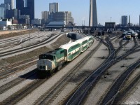 GO Transit GP40-2W 709 trails an inbound commuter train of three bilevels and an APCU (F-unit converted into a cab car/HEP car) heading to Union Station in downtown Toronto, passing by VIA's former CN Spadina coachyard at Bathurst Street. VIA LRC locomotives are visible heading up consists on the yard tracks, and a CN S13 used for switching passenger cars sits in one of the sidings. Self-propelled VIA RDC's sit near the old steam-era coal tower, beyond which is Spadina Roundhouse where VIA's locomotives are serviced.
<br><br>
The 1980's were a transition period for Toronto's old steam-era rail facilities downtown, as the VIA (former CN) Spadina Roundhouse and coachyard would both soon close and move to new facilities in Mimico, and the lands here would be cleared for redevelopment, including for the future Skydome (presently the Rogers Centre). The old CN freight yards at Bathurst Street (on the left) have been converted for storing GO trains, and the new flyunder between Bathurst Street and Spadina Avenue (behind the train) has been completed.