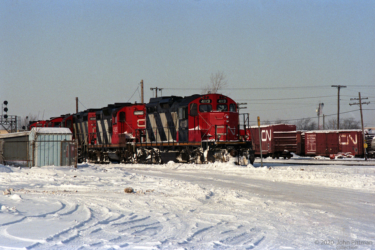 CN 4113 is a GP9 remanufactured at Pointe St-Charles in Montreal; short hood chopped becoming front end, etc. 
Behind it are an as-built GP9 CN 4385, GP9rm CN 4129, an SW1200RS, and yard GP9rm CN 7034.
At the left can be seen CN Dundas sub signal 765N.
On the right side are some double-door boxcars, including CN 73421 (re-numbered for non-revenue service).
Submitted during a summer heat wave in Ontario, inspired by the question: "Why can't it snow in July when we need it?"