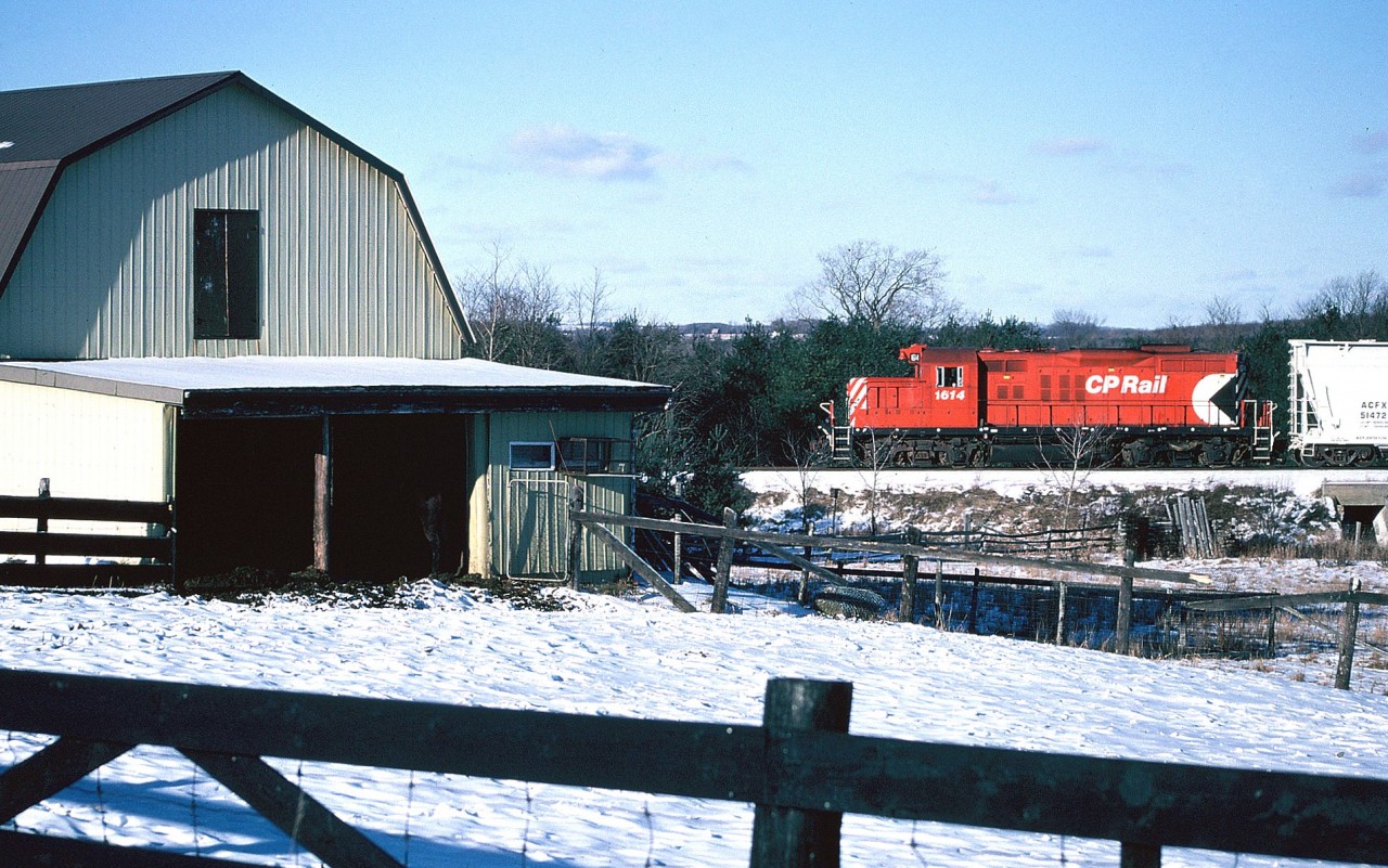 The last CP train to operate to Guelph on the Goderich Subdivision approaches the hamlet of Arkell. GP9u 1614 and one hopper are passing a barn along Watson Road where even the animals wouldn't dare venture outside due to the frigid temperatures that day.