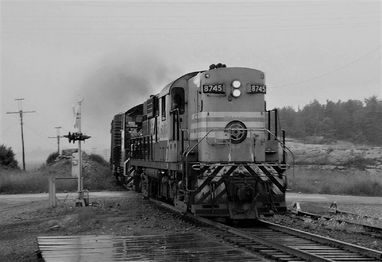 The rain has finally stopped as CP RS-18 8745 and SW1200RS 8171 lead a short train over Lake Huron Drive in the small town of Desbarats as they continue their journey to Sault Ste Marie.  The mileage indicated is approximate.