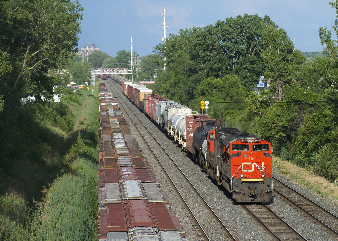 A 44-car CN 323 has CN 8014 and CN 5668 for power as it approaches Taschereau Yard. Grain cars can be seen on the three other tracks of CN's Montreal Sub. Parked grain cars are at far left on the transfer track and receding into the distance are the tail ends of CN 596 with a short transfer of grain cars on the freight track and grain train CN 878 at far right on the south track.
