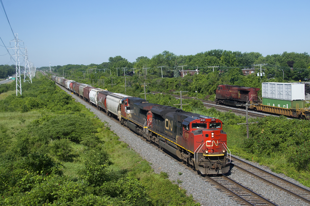 CN 322's head end and CP 112's rear DPU are pacing each other as they approach a pedestrian overpass in Beaconsfield. CN 322 has 160 cars and weighs in at nearly 20,000 tons, with most of the train consisting of grain cars for Montreal. Power is CN 8101 and IC 2465 up front and CN 2288 and CN 2441 mid-train, CN 2441 being one of the few CN cowls currently in service.
