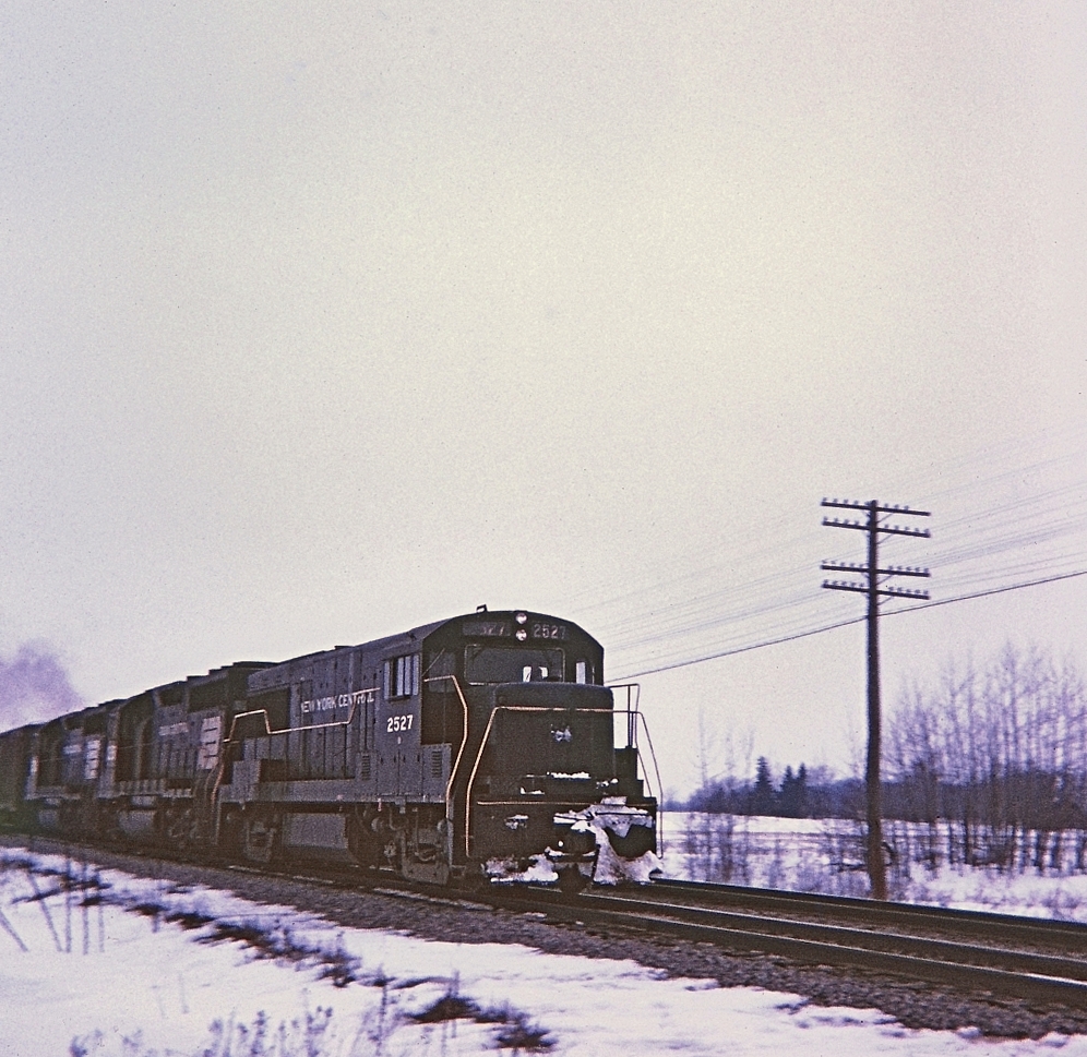 On the CASO sub, hotshot train NY-4 with a GE U25B NYC 2527 leading is about to bang over the diamond at E&O tower. Trailing in the consist were PC 3258 and 3026. Note the "one piece" front windshield on 2527. It is hard to comprehend that this great double track mainline as well as the TH&B Dunnville sub are all ancient history now.