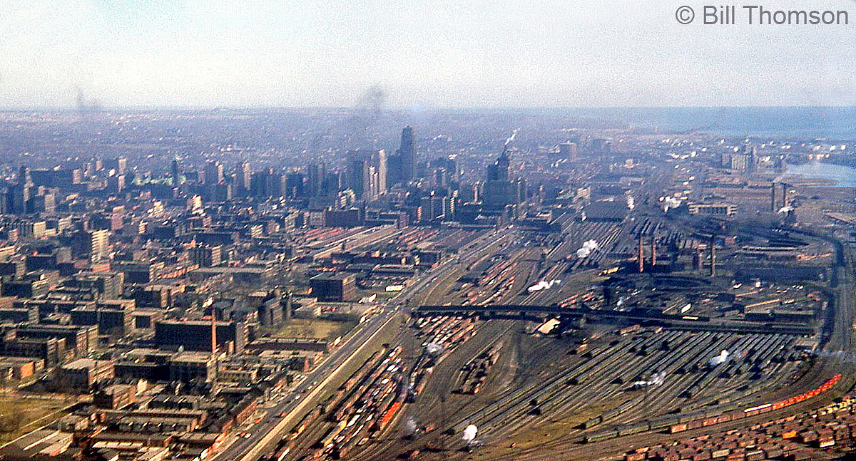 An aerial view of the downtown railyards in Toronto from 1953 yields a very different picture than today. Taken from the air looking east near Bathurst Street, Spadina Avenue is visible crossing over the railway yards. Steam is still dominant, and one can count the white puffs of smoke from many of the steam engines working around the yards. Notable former railway landmarks are CN's Spadina Coachyards, CN's Spadina Roundhouse, CP's John Street Roundhouse, the "High Line" freight byoass running south of both roundhouses (on the right), Union Station, and the CN & CP freight sheds north of Front Street.The steam era ended on Canadian railways at the end of the 1950's, but the steam era facilities in downtown Toronto continued servicing passenger equipment and locomotives here until they were either closed down or moved to more modern facilities in the 1980's, clearing the way for redevelopment of the old downtown "railway lands" in the following decades.  Some more downtown Toronto photos:Alternate angle in 1953: http://www.railpictures.ca/?attachment_id=23318Looking east from Spadina Avenue: http://www.railpictures.ca/?attachment_id=28556Steam at Spadina Roundhouse: http://www.railpictures.ca/?attachment_id=24444John Street roundhouse, Union Station & the Royal York Hotel: http://www.railpictures.ca/?attachment_id=38504Spadina Roundhouse in 1980: http://www.railpictures.ca/?attachment_id=32212Bathurst St. in 1987: http://www.railpictures.ca/?attachment_id=41906