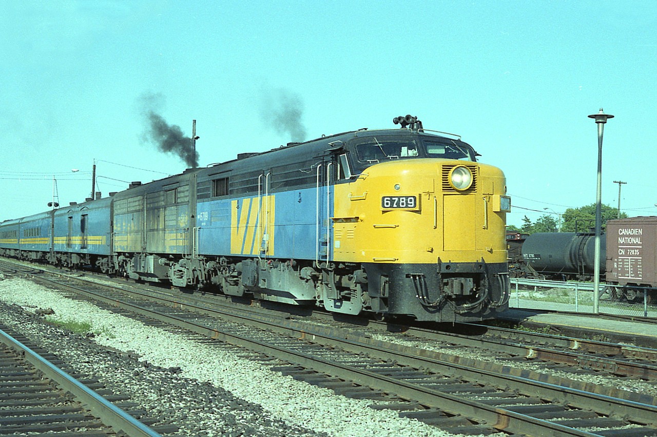 It is a beautiful day, a Thursday afternoon and because it is a weekday VIA's 75 westbound is not all that big. Just 8 cars. This scene is at the old Freeman Station at Burlington West, and the train is stopped to take on passengers. Behind VIA 6789 is 6867. The leader retired by 1989. Don't know where it went. Scrapper? At least the 6867 was saved. It went to Danbury, CT rail museum.