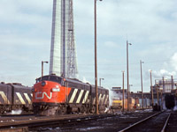 Construction is nearing completion on what would be the world's tallest freestanding structure (until 2007).  The CN Tower will open a little over a year later in June 1976.  Meanwhile far below, locomotives idle on the Spadina engine service tracks including CN 6529, (GMD FP9A, 1957) and an unknown MLW FPB4.  At left a pair of GMD cab units, only FP9A 6542 (1958) identifiable, what appears to be the rear of an MLW FPA cab unit at right, and in the distance near the boarded up roundhouse, an ONR FP7A unit.<br><br>The Spadina roundhouse was built by Canadian National Railways in 1928 and was home to various <a href=https://rockontrains.files.wordpress.com/2018/09/cnr-6233-5296-spadina-roundhouse-toronto-ont-9-15-58-credit-ron-wright.jpg?w=848>steam and diesel power</a> off the passenger trains and for local switching duties.<br><br>CN 6529 and 6542 were transferred to VIA Rail April 1, 1978 at the start of national passenger operations.  6542 would continue in service until 1994 when it was sold to General Scrap in Winnipeg.  6529 was rebuilt by Pointe Ste Charles shops in 1984 and renumbered to <a href=http://www.railpictures.ca/?attachment_id=23638>VIA 6311</a>, later modified by in 1997 to replace the steam generator with a head end power generator for use out of Winnipeg on the <a href=http://www.railpictures.ca/?attachment_id=7695>Churchill run</a>.  It would later be sold in 2002 to IFE Leasing to work for the Washington and Idaho Railroad (WIR) as <a href=http://www.trainweb.org/oldtimetrains/photos/cnr_diesel/KRLX_6311.jpg>MRLX, later KRLX  6311,</a> wearing the Southern Pacific <a href=https://i.pinimg.com/originals/3b/ba/99/3bba995af8afe0e9d865ac098b13be9b.jpg>2-tone gray 'Lark' scheme,</a> worn by the railroad's Cascade, Lark, and Overland trains.  The unit returned to Canada in 2014 as <a href=http://www.railpictures.ca/?attachment_id=34316>RPCX 6311,</a> now residing at the Alberta Railway Museum in Edmonton.