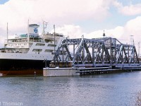 The bridge tender has moved the swing bridge carrying Penn Central's Canada Division line (the CASO) into the open position to let a ship pass through the Welland Canal during a visit in December 1969, resulting in a brief pause in rail traffic. Increasing levels of ship traffic through the canal was one of the reasons that lead to the new canal alignment and construction of the Townline Tunnel, which opened a few years later and ran underneath the canal, eliminating interruptions in mainline railway traffic for marine traffic. The PC mainline was also shifted south as part of the track alterations for the new canal and tunnel.